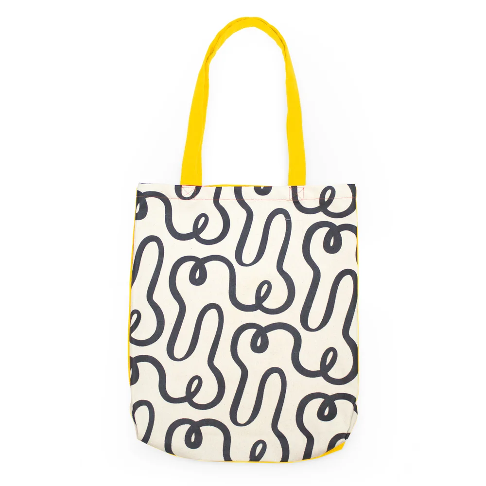 Cream canvas tote with a soft black squiggle pattern and warm yellow straps, photographed on a clean neutral surface